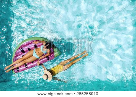 Two people (mom and child) relaxing on watermelon lilo in the pool at private villa. Summer holiday idyllic. High view from above.