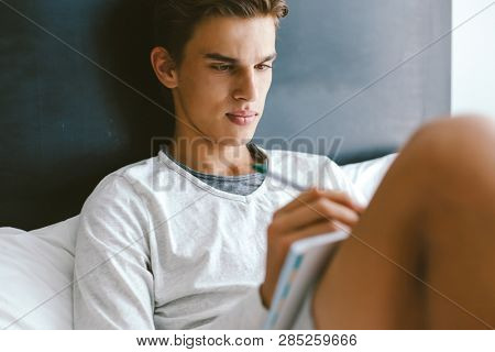 16 years old teenage boy prepare for exams while relaxing on couch in his room