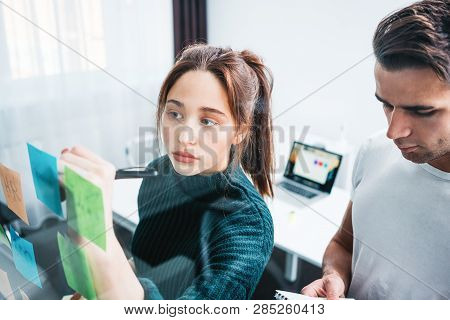 Portrait Of Two Coworker People Standing At Office Space Behind Glass Wall With Sticky Notes. Team O