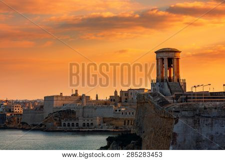 View of Siege Bell War Memorial as old walls and fortress on background under beautiful evening sky in Valletta, Malta.