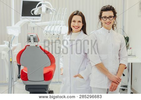 Two Doctor Dentist In The Office. Beautiful Young Women. Standing With A Touch Of One Another. Look 