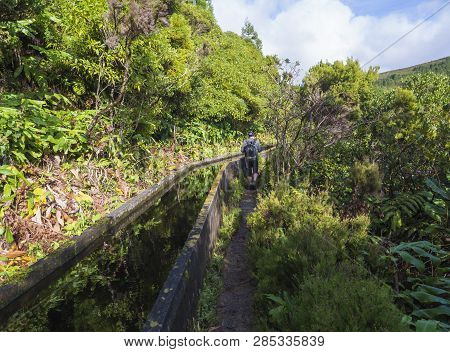 Men Hiker Walking On Footpath Along Lavada - Water Irrigation Canals Covered By Moss And Lush Vegeta
