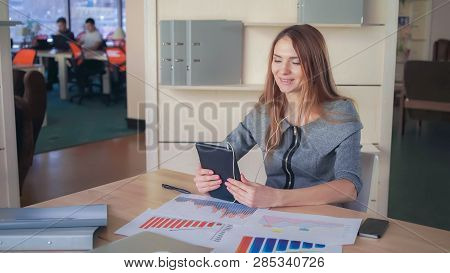 Business Woman Using App On The Touch Screen Tablet. On Her Desk Documets And Charts With Sales Repo