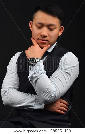 A Thoughtful Young Asian Man Has Put A Hand With A Clock To Face, Looks Down