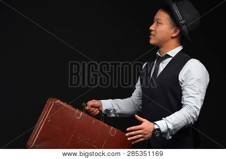 Asian Young Man In A Hat With A Brown Suitcase, And Raises His Arms Looking Sideways
