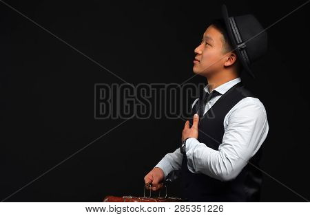 Asian Man In A Black Hat Turned Aside, Looking Sideways On A Black Background