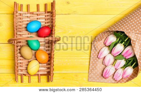Colorful Bright Eggs And Bouquet Fresh Tulip Flowers On Yellow Background Top View. Spring Holiday. 