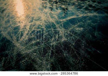 Surface of outdoor ice with sun reflection, replete with skate marks.
