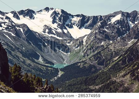 View From The Top Of The Valley With A Beautiful Lake Between High Mountains With Snow Caps. The Riv