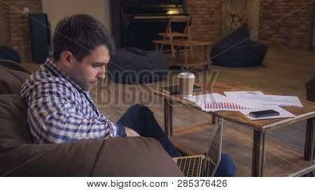 Attractive Man In A Plaid Shirt Sitting On The Couch, On Your Feet Is A Laptop, Male Servite Interen
