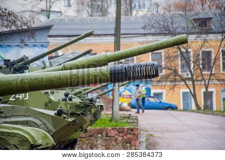 Row Of Numbers Of Military Blow Guns, Cannons, Howitzers Against The Backdrop Of Peaceful Multi Apar