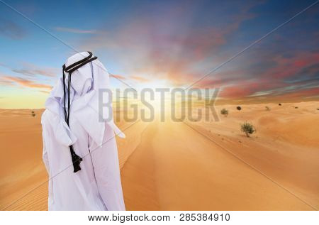 Arabic man with traditional emirates clothes in the desert, sunset.