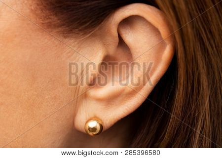 health, people and hearing concept - close up of senior woman ear with golden earring