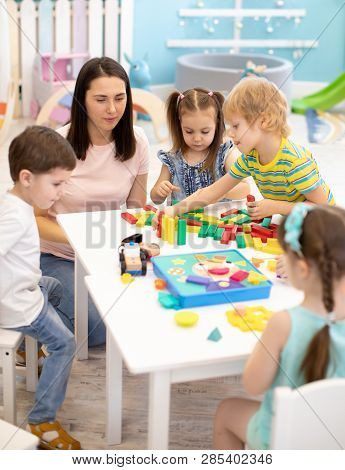Little Children Playing Different Toys With Teacher In Daycare. Kids Building Color Blocks. Educatio