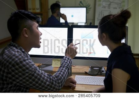 Business People Discussing Digrams On Glowing Computer Screens In Dark Office