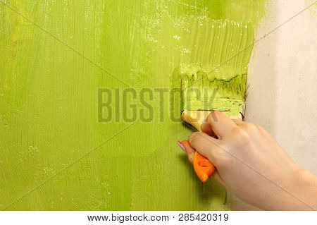 Female Hand With A Flat Brush With Green Paint Paints The Wall At Home