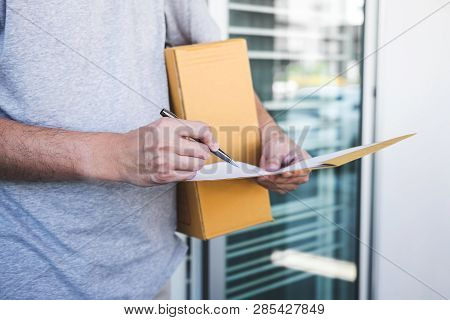 Delivery Mail Man Giving Parcel Box To Recipient, Young Man Signing Receipt Of Delivery Package From