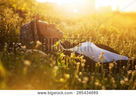 Happy Girl In A Hat Lies Among The Meadow Flowers And Dreams Of Something