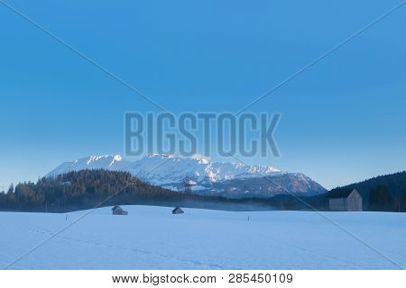 Some Snow Covered Small Huts On A Field With Mountains Grimming, Schartenspitze And Steinfeldspitze 