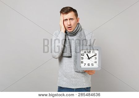 Preoccupied Young Man In Gray Sweater, Scarf Put Hand On Head Hold Square Clock Isolated On Grey Bac