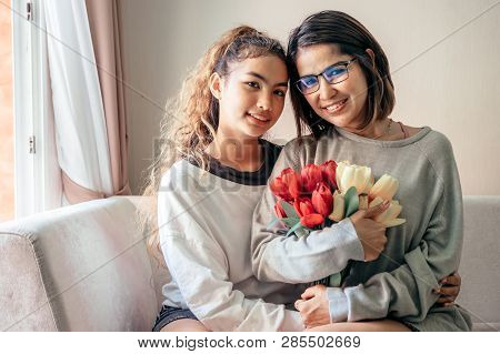 Senior Mom And Her Daughter Are Hugging, Smiling And Dringking A Warm Coffee In Some Morning.