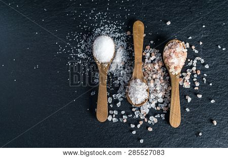 Different Types Of Salt. Sea, Himalayan And Kitchen Salt. Top View On Three Wooden Spoons On Black B