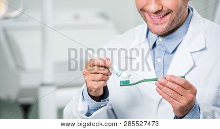 Cropped View Of Happy Male Dentist Squeezing Toothpaste On Toothbrush In Dental Clinic