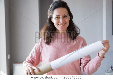 Smiling Female Architect Pulling Rolled-up Drawing Out Of Tube. Pretty Woman Looking At Camera And H