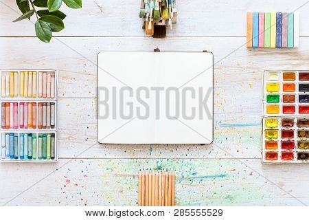 Paint Brushes Set, Paintbox With Watercolors, Crayons, Pencils And Open Notebook Paper On White Wood