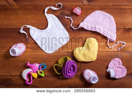 Baby Clothes Accessories Set, Pink Knitted Cotton Clothing, Toys And Kid Bib On Brown Wooden Backgro
