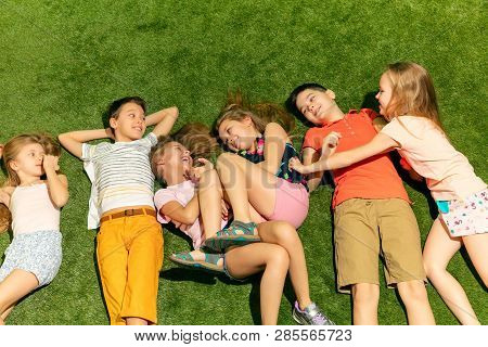 Group Of Happy Children Playing Outdoors. Kids Having Fun In Spring Park. Friends Lying On Green Gra