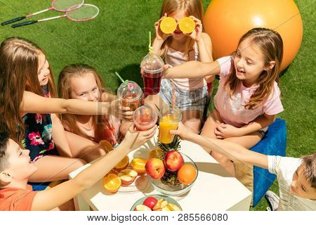 Kids Fashion Concept. The Group Of Teen Boys And Girls Sitting On Green Grass At Park. Children Colo