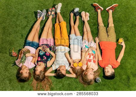 Group Of Happy Children Playing Outdoors. Kids Having Fun In Spring Park. Friends Lying On Green Gra