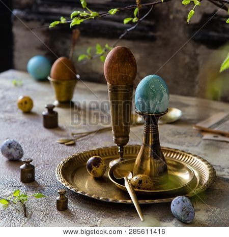 Easter Eggs Painted With Natural Dyes Standing On Brass Golden Stacks And Plate On Concrete Backgrou