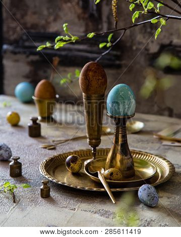 Easter Eggs Painted With Natural Dyes Standing On Brass Golden Stacks And Plate On Concrete Backgrou