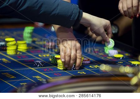Roulette Table With Human Hands Putting Down Chips In Casino. Roulette Wheel In The Foreground. Gamb
