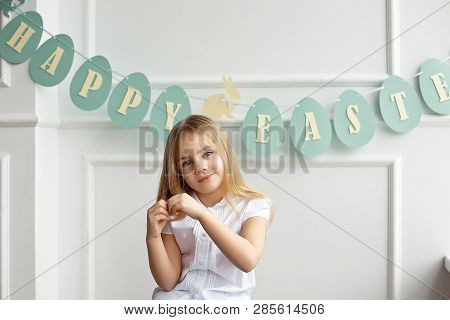 Cute Little Blonde Girl Sitting In A Bright Room Near The Window On The Background Of Streamers With