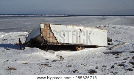 abandoned trailer under the snow at the edge of a river