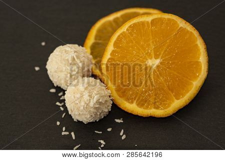 Close Up Of Rafaello Homemade Delicious Candy Sitting Next To Fresh Orange Slices. Healthy Natural D