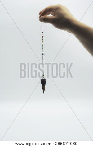 Pendulum Dowsing On An Isolated White Background With A Seven Colored Chakra Crystal Point.