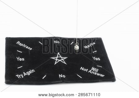 Pendulum Dowsing On An Isolated White Background With A Silver Point And A Black Dowsing Matt.