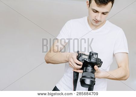 A Young Man Holds A Photo Camera In His Hand And Looks At The Photo On The Photo Camera. Isolated Gr
