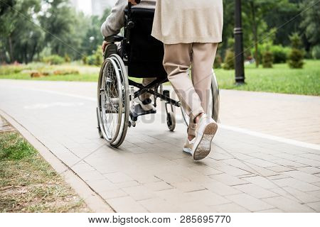 Partial View Of Senior Woman Carrying Husband In Wheelchair While Walking In Park