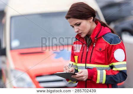 Concetrated Female Paramedic In Uniform Writing In Clipboard