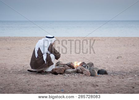Authentic Bedouin With White Kufia On His Head On The Red Sea Coast Sits By The Hearth