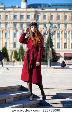 Full body portrait. Young beautiful brunette woman in stylish in a long burgundy coat walking in spring street