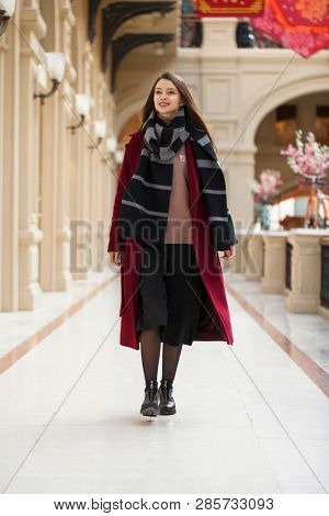 Full body portrait. Young beautiful woman in stylish in a long burgundy coat, indoor shop