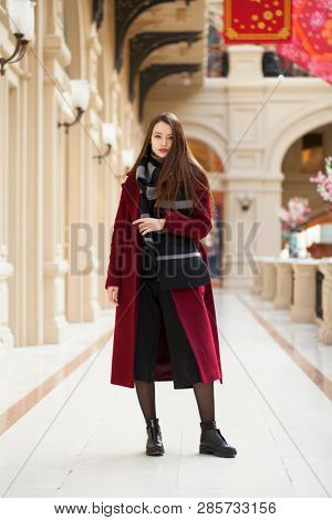 Full body portrait. Young beautiful woman in stylish in a long burgundy coat, indoor shop