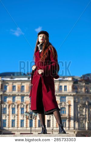 Full body portrait. Young beautiful brunette woman in stylish in a long burgundy coat walking in spring street