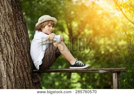 Boy In Shorts And A Hat Sits On A Bench